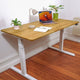 Höhenverstellbarer Schreibtisch - Eiche Natur White in einem Raum stehend. Eingerichteter, ergonomischer Home-Office Arbeitsplatz mit Fokus auf Eleganz und natürliche Holzoptik. Schrägansicht.
