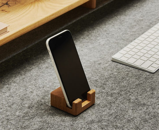 Smartphonehalter aus massivem Eichenholz mit Korkelement, der ein Smartphone aufrecht und griffbereit auf dem Schreibtisch hält.