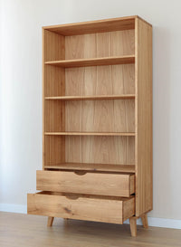 Schrägansicht von Bücherregal aus Massivholz Eiche an der Wand stehend und mit geöffneten Schubladen