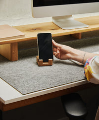 Smartphonehalter aus massivem Eichenholz mit Korkelement, der ein Smartphone aufrecht und griffbereit auf dem Schreibtisch hält.